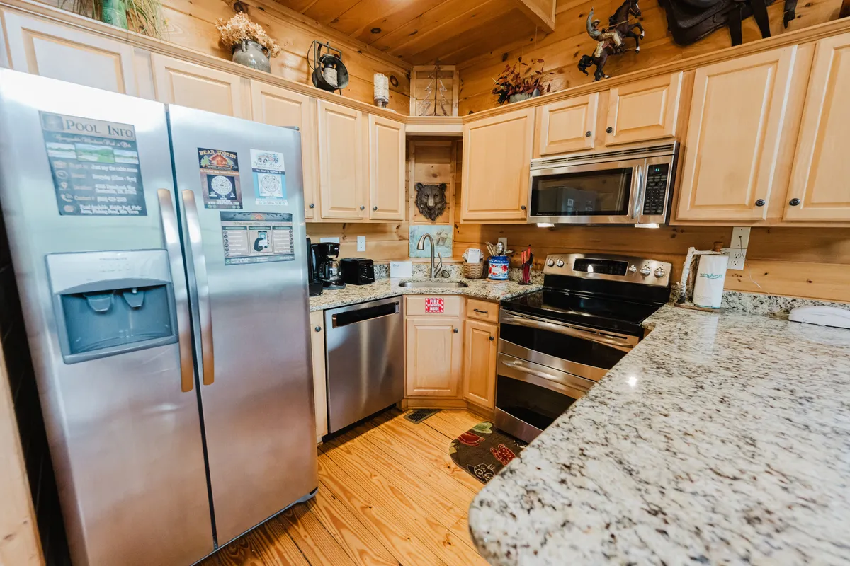 A welcoming kitchen scene featuring a stainless steel refrigerator, granite counters, wooden cabinetry, and modern appliances. The lighting highlights the spacious prep area and the inviting atmosphere, ideal for cooking and casual gatherings.