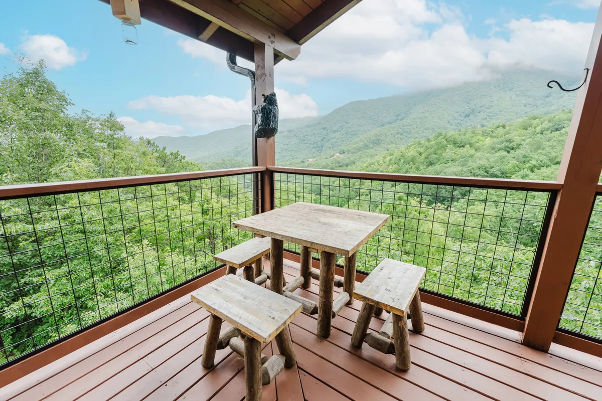 An outdoor wooden table with stools sits on a deck overlooking a stunning mountain view. The space is perfect for outdoor dining, morning coffee, or winding down after a day at nearby theme parks.