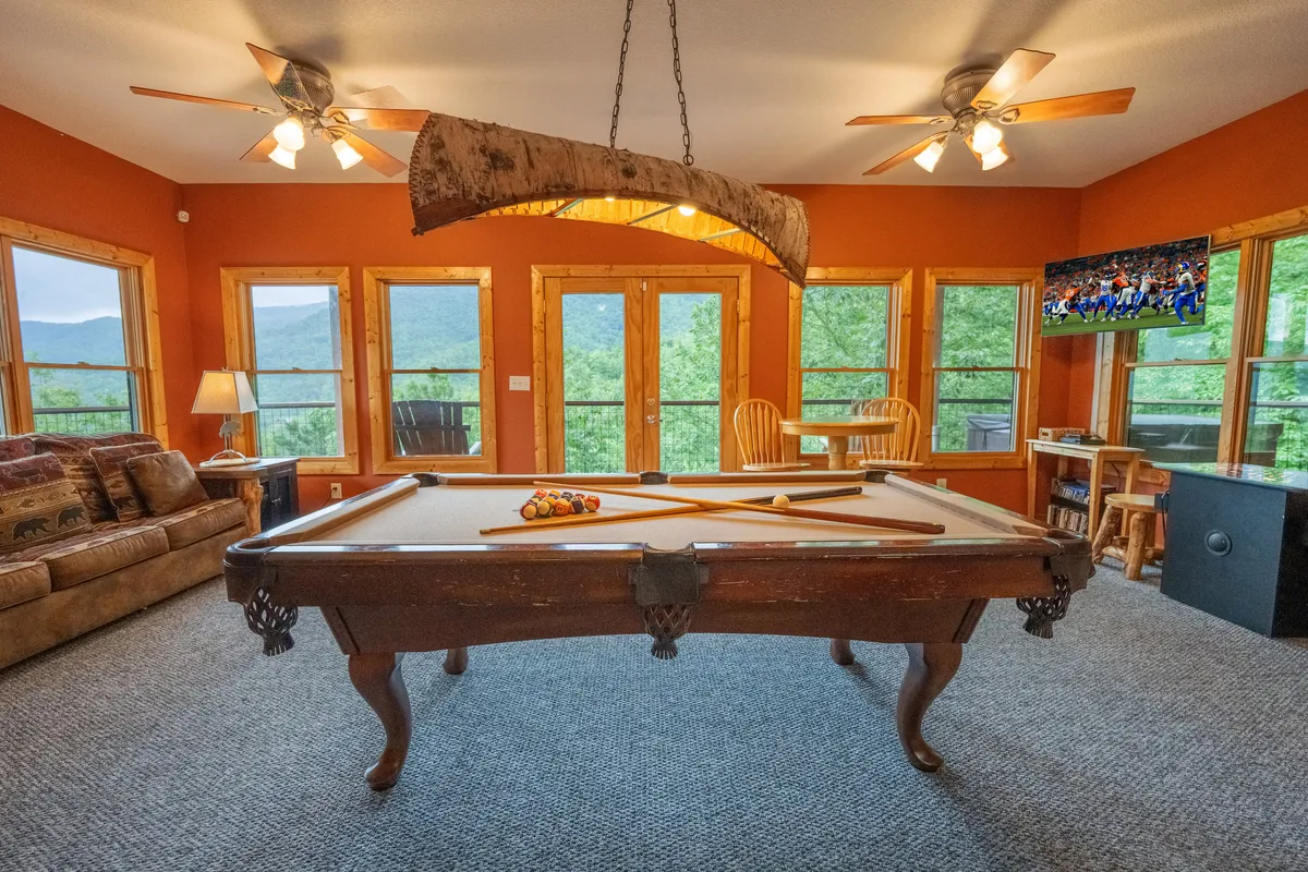 A lively game room featuring a pool table, comfortable seating, and large windows that offer plenty of natural light. The television and casual arrangement make it perfect for entertainment and friendly competition.