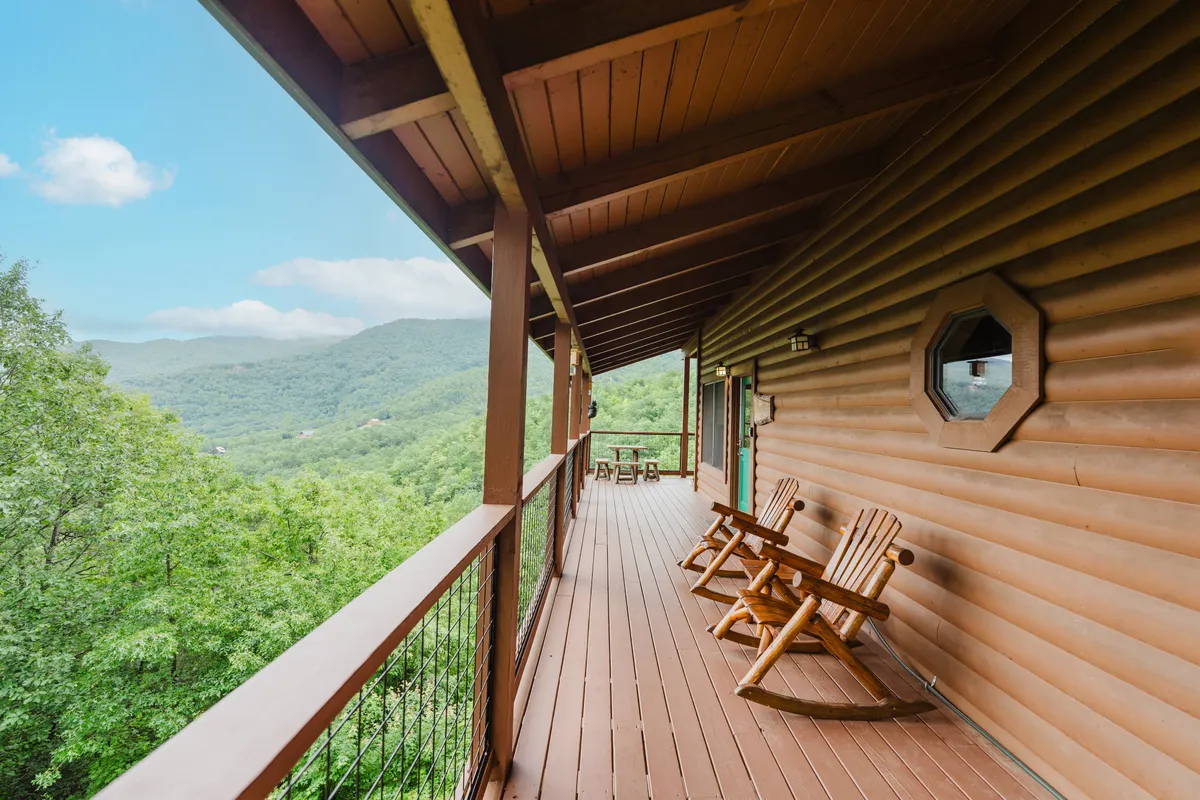 A close-up of a wooden deck featuring classic rocking chairs overlooking a magnificent, unobstructed mountain landscape. The tranquil setting invites guests to relax, recount their adventures, or simply soak in the sunrise or stargaze at night.