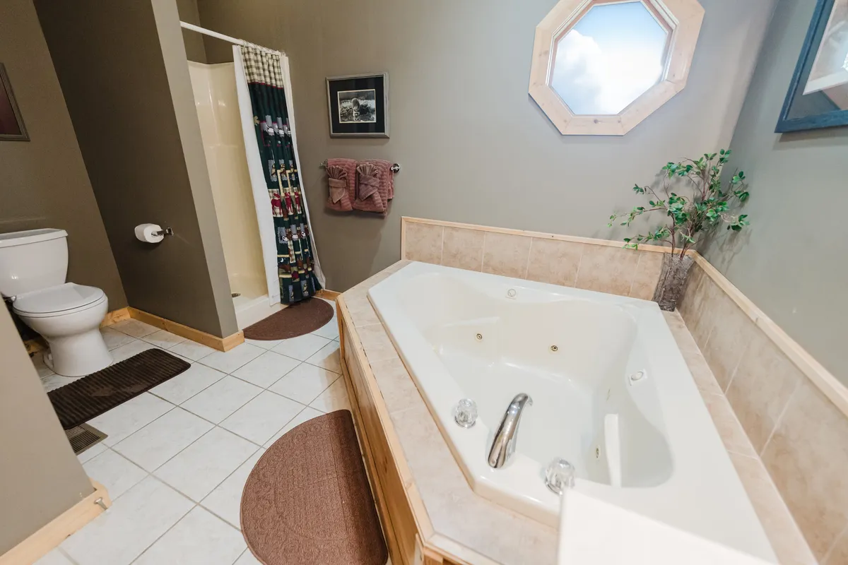 The master bath features a luxurious jacuzzi tub beneath an octagonal window, surrounded by decorative plants and a toilet nearby. Natural light brightens the space, evoking a tranquil, spa-like atmosphere.