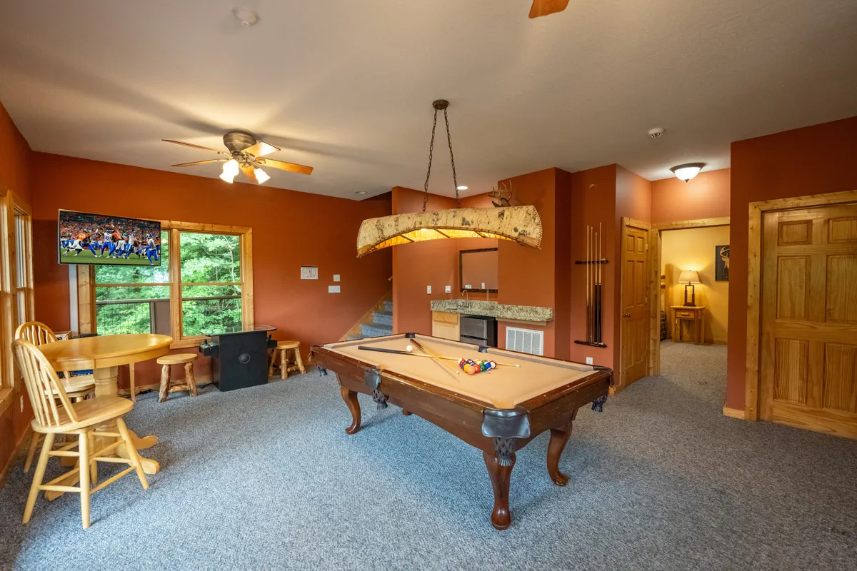 A vibrant entertainment space showcasing a pool table, TV, and a cozy bar area with wooden chairs. The casual setup invites guests to play games, watch sports, and enjoy snacks or drinks together.