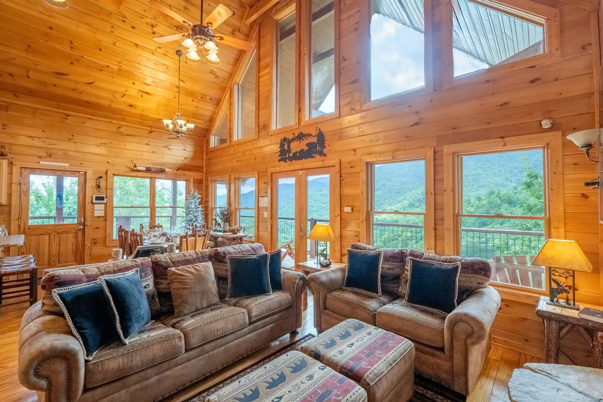 A cozy living area with comfortable sofas and large windows that frame the mountains beyond. Rustic wooden décor and warm lighting create an inviting ambiance ideal for gathering with loved ones, celebrating holidays, or simply relaxing while watching the changing weather and foliage outside.