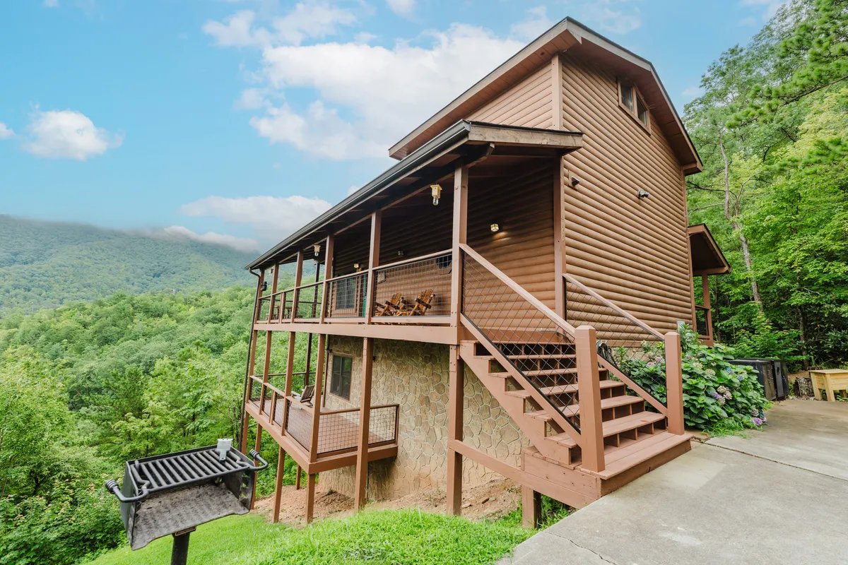 A spacious wooden deck equipped with a grill area and outdoor dining furniture, all set against the backdrop of rolling mountains. The inviting setup suggests opportunities for outdoor meals, socializing, and enjoying the sublime surroundings.