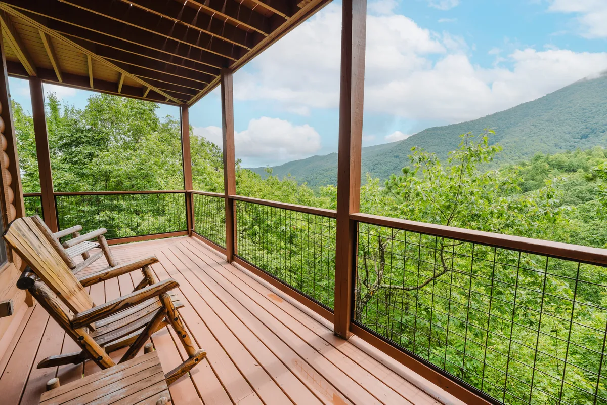 A wide shot of the deck showing the wooden rocking chairs prominently placed to enjoy a sweeping, unobstructed mountain panorama. The wooden structure and railing frame the view, inviting guests to imagine themselves savoring quiet, romantic moments in nature.