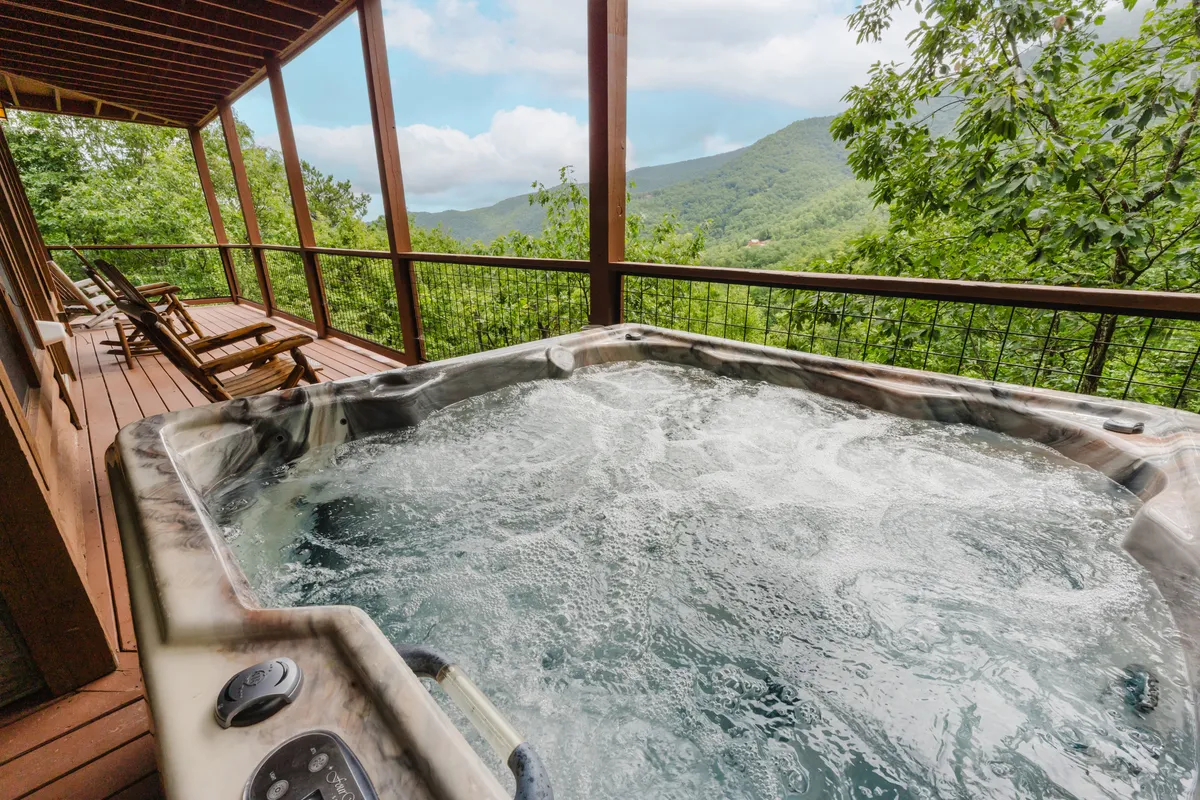 This exterior image showcases a wooden deck featuring a private hot tub set against a breathtaking mountain backdrop. The bubbling water, sturdy deck, and sweeping views invite relaxation and highlight the promise of unwinding outdoors. The setting is ideal for soaking in nature's beauty at sunrise or sunset.
