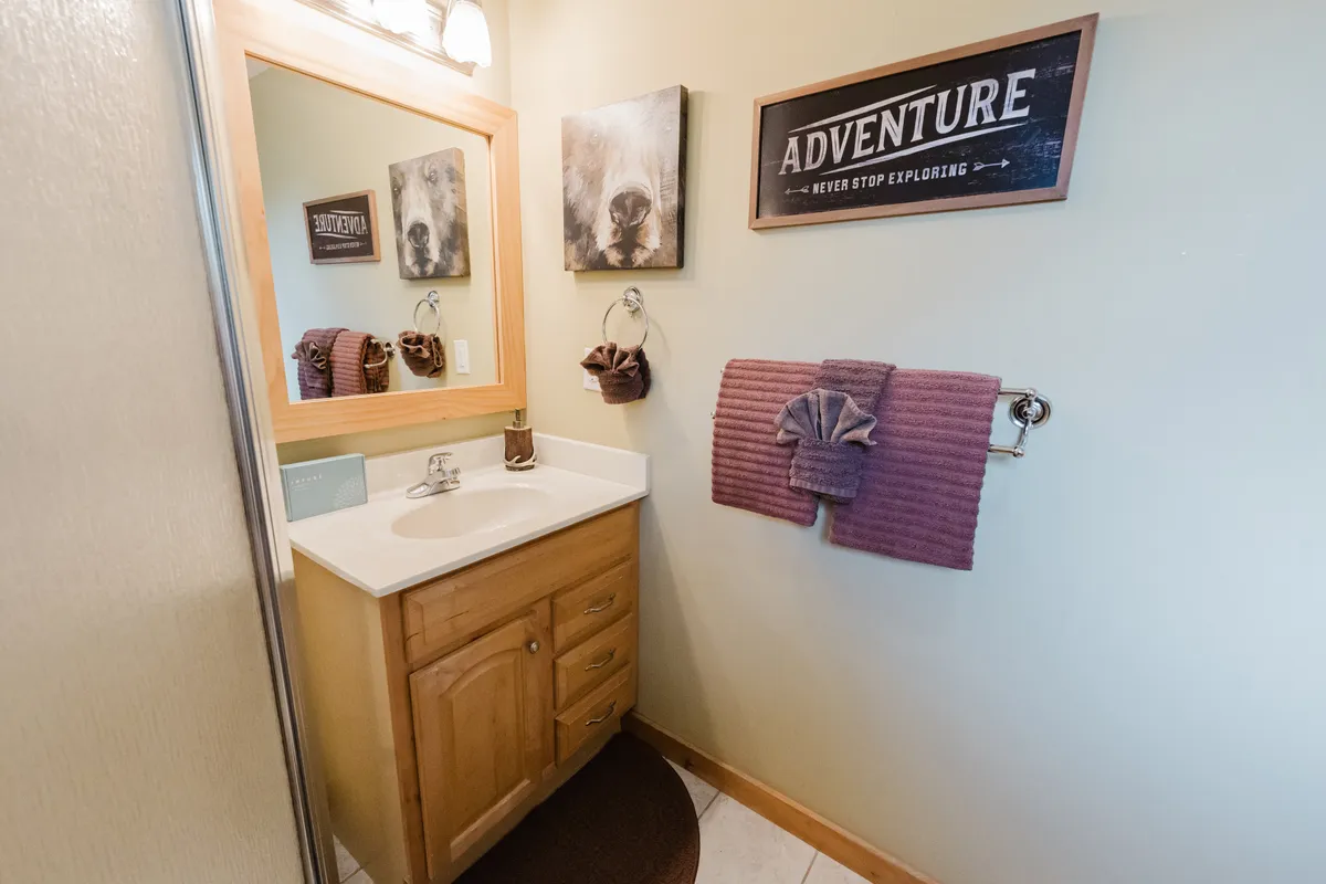 A fresh, inviting bathroom scene with a sink, wooden cabinetry, mirror, framed artwork, and plush towels. Bright lighting and organized amenities create a welcoming, functional space for daily routines.