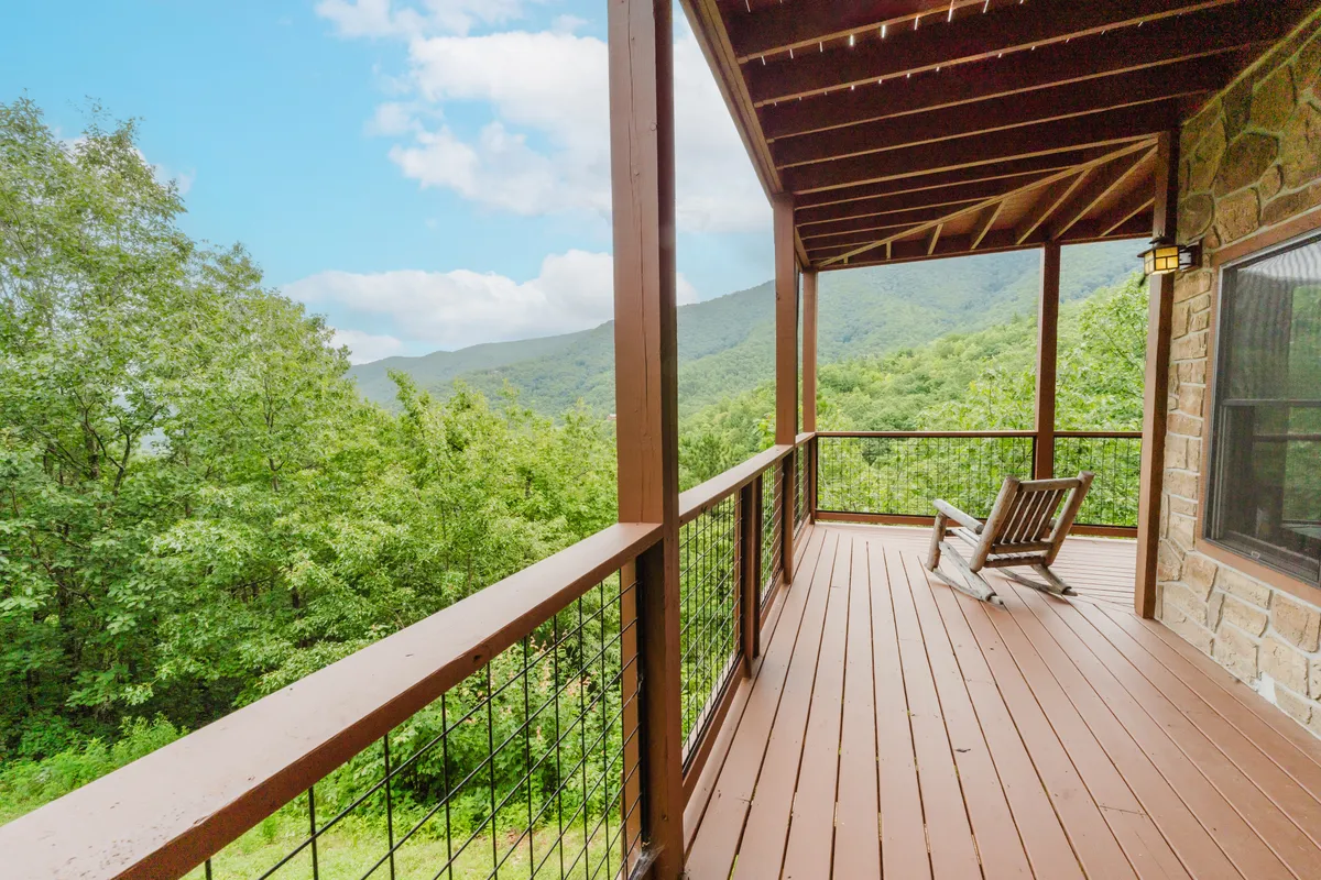 A tranquil wooden deck furnished with a classic rocking chair overlooks a sweeping mountain vista. The gentle morning light casts a warm glow, while the lush surroundings hint at the changing beauty of each season. The setting exudes serenity, inviting visitors to soak in the views, whether watching sunrises or enjoying crisp mountain air.